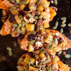 Baking sheet of sweet potato halves topped with softened apples, dried cranberries, pumpkin seeds, and pecans.