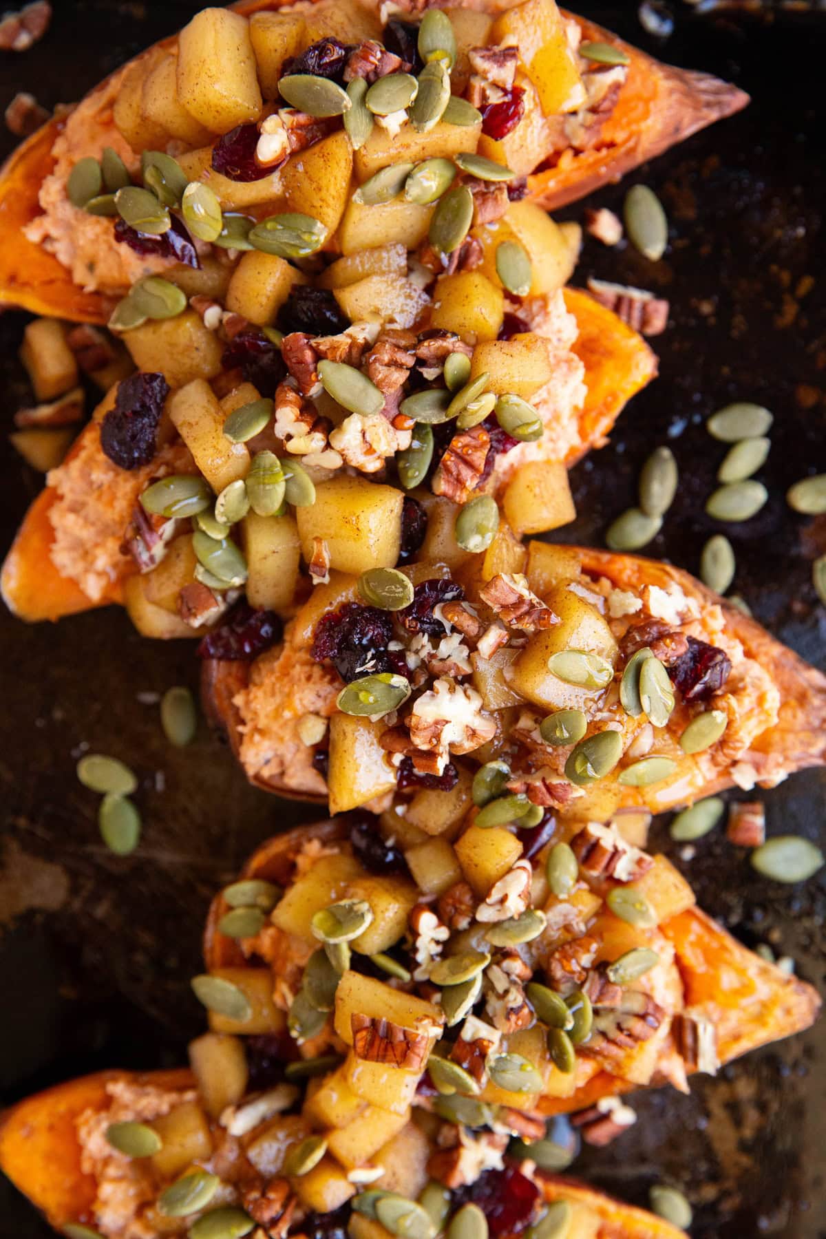 Baking sheet of sweet potato halves topped with softened apples, dried cranberries, pumpkin seeds, and pecans.